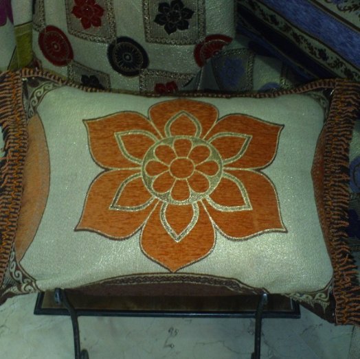 Housse de coussin marocaine jaune orangé ornée de motifs en fleur et cernée d'un liseré.